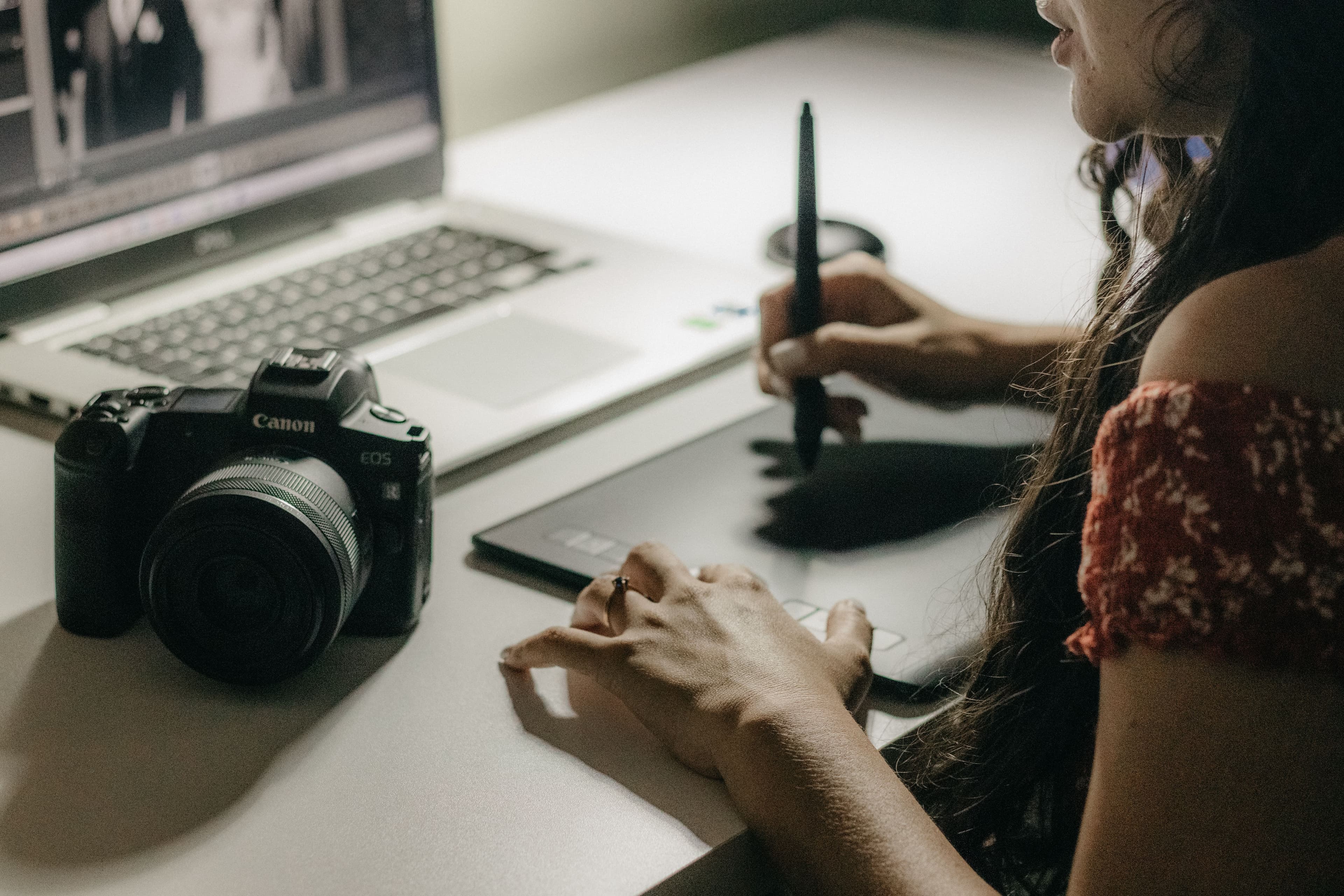Une photographe travaille sur son ordinateur à son bureau, avec une tablette graphique et un appareil photo à côté.
